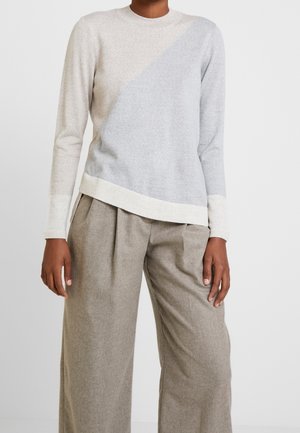 Persona que lleva un suéter de manga larga con bloques de color beige y gris claro y pantalones anchos de tiro alto en color topo.