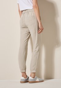 Linne joggerbyxor i ljusbeige med elastisk midja, avsmalnande benslut och två bakfickor; matchat med grå och vita sneakers.