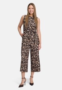 Beige és fekete leopárd mintás overall, ujjatlan dizájn, övvel a deréknál, széles, bokáig érő lábak, fekete magassarkú cipővel párosítva.