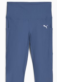 Blå atletiska leggings med bred midjeresår, sidfickor och subtila sömdetaljer. Har en liten vit logotyp på vänster sida.