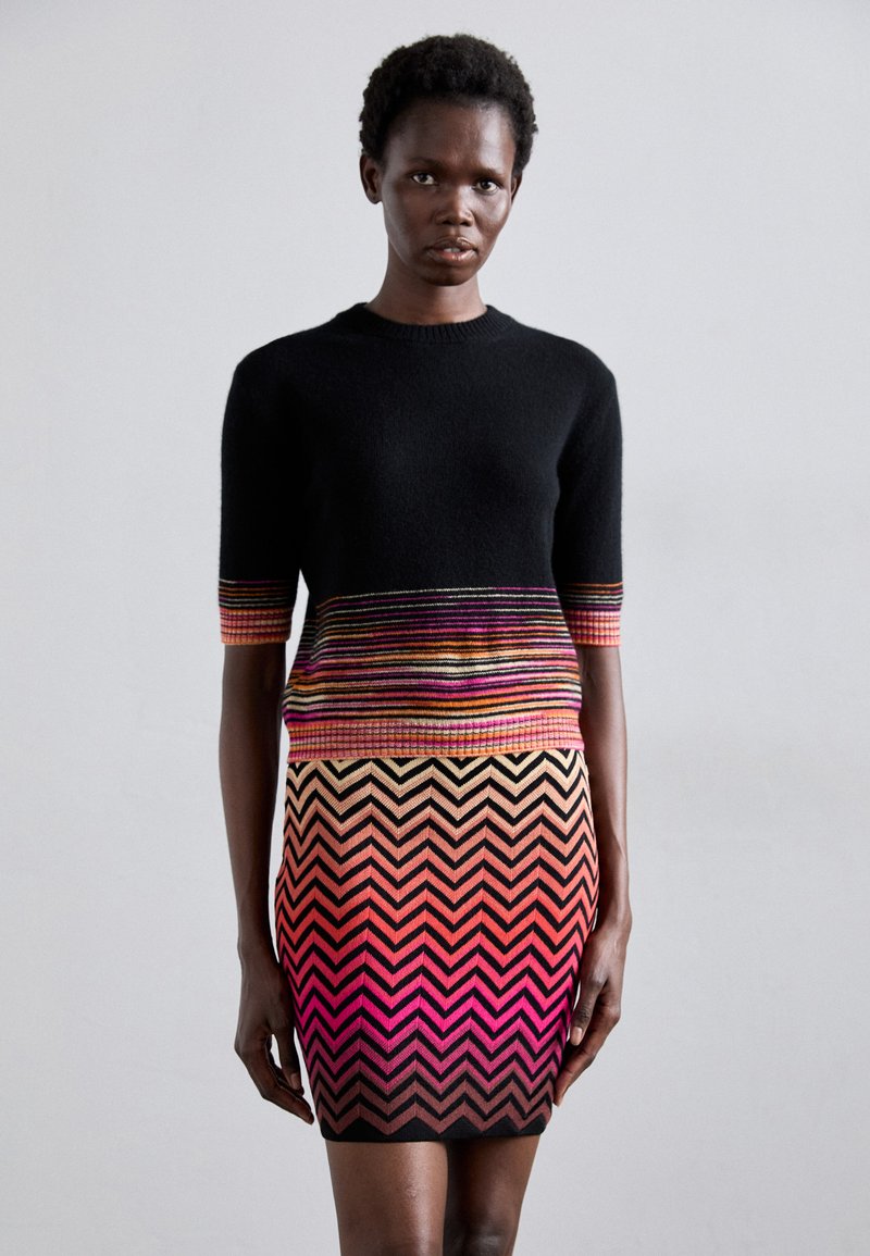 Sweater preto de malha com mangas curtas, apresentando um padrão de riscas multicoloridas, emparelhado com um vestido ajustado em padrão de zigue-zague com tons em gradiente.
