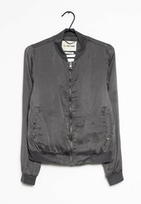 Šedá bomber bunda s předním zipem, vyrobená z lesklé tkaniny. Má žebrovaný límec, manžety a dvě boční kapsy.