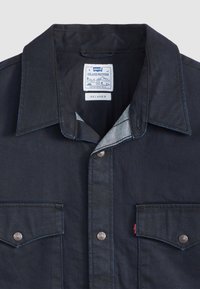 Dark denim western shirt featuring a pointed collar, snap buttons, chest pockets, and contrasting stitching details. Label: Levi's Relaxed.