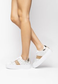 Białe sneakersy z wzorzystą cholewką i złotymi akcentami. Posiadają teksturowaną podeszwę i metalowe detale na pięcie. Zapięcie na sznurowadła.