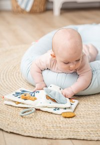 Zacht stoffen babyboek met kleurrijke ontwerpen van zee dieren, een blauwe getextureerde klep en een siliconen bijtring, op een getextureerde beige mat.