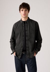 Dark gray denim shirt with button closure, pointed collar, and long sleeves. Worn over a black T-shirt, paired with blue denim pants.