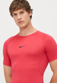 Rdeča kratkolabračna športna majica iz raztegljive tkanine, z črným logotipom Nike na prsih in aerodinamičnimi šivi za prilegajoč videz.