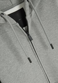 Szara bluza z kapturem na zamek, wykonana z miękkiego materiału, z czarnym zapięciem na zamek i sznurkiem z czarnymi końcówkami, o gładkim, teksturowanym wykończeniu.