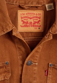 Brązowa kurtka Levi’s z metalowymi guzikami, przednimi kieszeniami, skórzaną naszywką Levi Strauss & Co. oraz metką "Made in Cambodia" wewnątrz kołnierza.