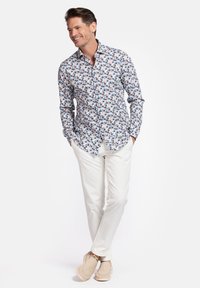 Heren overhemd met knopen in het wit met een meerkleurig bloemenpatroon. Gecombineerd met lichtbeige broek en schoenen, met een ontspannen pasvorm.