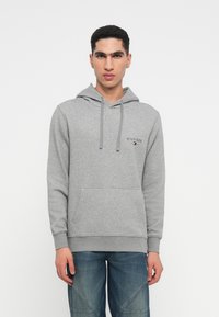 Gray cotton hoodie with a front pocket, drawstring, and logo detail on the chest, paired with blue jeans featuring a textured pattern.