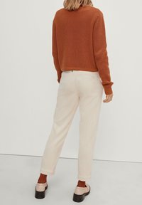 Rostfarbener Strickpullover mit einem cropped Design, kombiniert mit kremfarbenen Cordhosen. Die Schuhe sind hellrosa mit einer klobigen schwarzen Sohle.