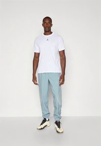 Wit Jordan T-shirt met klein zwart logo, gecombineerd met lichtblauwe joggers met een patroonaccent. Draagt zwarte en crèmekleurige sneakers.