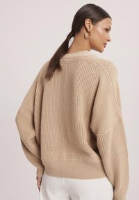 Beżowy sweter dziany o luźnym kroju, z opadającymi ramionami i ściągaczami. Posiada strukturalny wzór oraz okrągły dekolt.