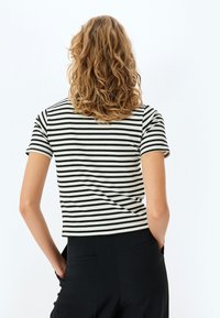 Top de manga corta a rayas en tejido de canalé blanco y negro. Presenta un escote redondo y una silueta ajustada, combinado con pantalones negros.