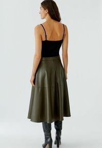 Débardeur noir ajusté avec des bretelles réglables ; associé à une longue jupe en cuir vert olive avec un design évasé et une fermeture éclair au dos.