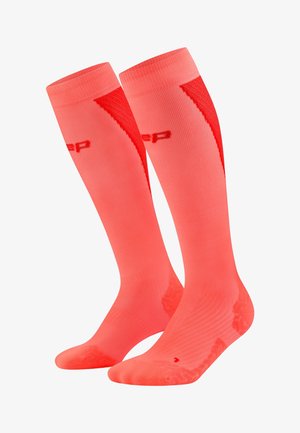 Een paar fel koraalkleurige kniehoge atletische compressiekousen met subtiele rode accenten en geribbelde boorden, zij aan zij weergegeven.