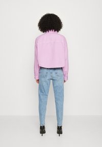 Rosa kort denimjacka med långa ärmar, med hög krage och synlig sömnad. Bärs tillsammans med ljusblå jeans och svarta klackar.