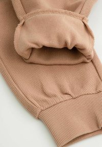 Jasnoróżowa bluza sportowa z teksturowanej tkaniny, z prążkowanymi mankietami i miękkim, marszczonym kapturem. Zbliżenie na detale i materiał.