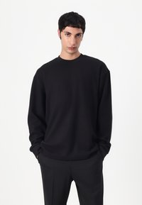 Sweat à capuche noir à coupe décontractée, avec un col rond et des manches longues, associé à un pantalon noir. Texture lisse avec un minimum de détails.