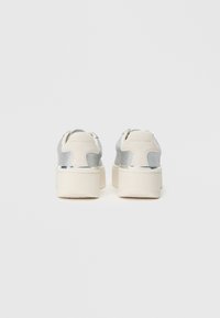 Baskets argentées texturées avec une épaisse semelle plateforme blanche, présentant un design élégant et des accents métalliques au niveau du talon.