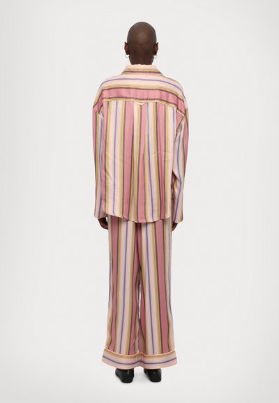 Striped pajama set in pink, featuring broad vertical stripes in various colors. Loose-fitting design with long sleeves and wide pants.