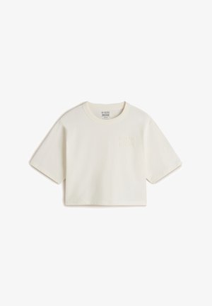 Camiseta blanca recortada de algodón, con cuello redondo y mangas cortas. Los detalles incluyen el texto en relieve "HECHA PARA LOS ELEMENTOS."