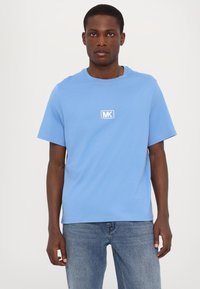 Lys blå bomull t-skjorte med korte ermer, rund hals, og en hvit brodert "MK"-logo på forsiden. Midjemodell, jevn tekstur.