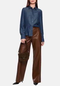 Denim button-up shirt with long sleeves, paired with high-waisted brown leather wide-leg pants. Includes a small brown suede handbag.
