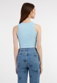 Top corto a coste blu chiaro abbinato a jeans blu a vita alta con motivi a cuore sulle tasche posteriori.
