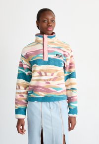 Fleece džemperis ar augstu apkakli, pasteļa joslu raksts rozā, zilā un krēma krāsā, ar pogām un logo uzplāksni uz krūtīm.
