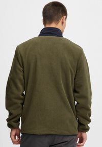 Fleece jacket in olive green with a high collar, soft texture, and long sleeves. Features a simple, clean design without visible hardware.