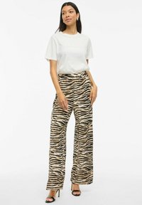 T-shirt blanc avec texte en relief associé à un pantalon large avec un motif rayé tigre beige et noir. Sandales à talons noires.