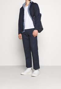 Granatowa bawełniana kurtka z denimu, biały t-shirt, granatowe spodnie i białe sneakersy. Minimalistyczny design z czystymi liniami i subtelną fakturą.