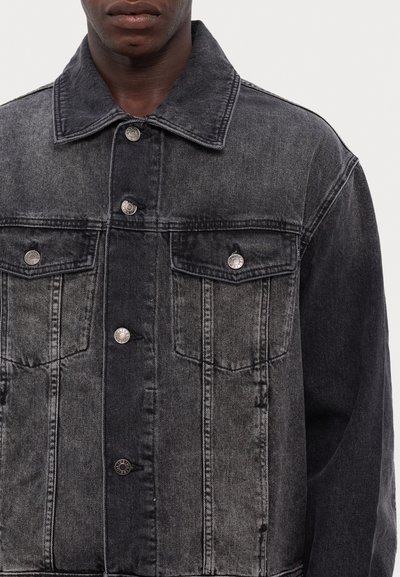 Black denim jacket with silver hardware, featuring two chest pockets, a button-up front, and a classic collar. Distressed texture detail.