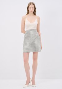 Beige tílko na tenké ramínka v kombinaci se světle modrou a bílou kostkovanou mini sukní. Modelka má na sobě bílé špičaté lodičky. Jednoduché pozadí.