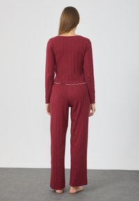 Bordeauxfärgad loungewear-set som består av en långärmad topp med rundad halsringning och ribbad textur, som kombineras med matchande byxor med utsvängd fåll.