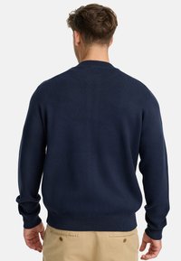 Suéter de punto azul marino con cuello redondo, puños y bajo acanalados. Presenta una textura suave y una silueta ajustada.