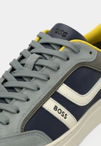 Γκρι σουέντ αθλητικά παπούτσια με ναυτικό δέρμα, λευκή ρίγα, κίτρινη λεπτομέρεια στη φτέρνα και υφασμένα γκρι κορδόνια. Διαθέτουν λογότυπο «BOSS» στη γλώσσα.