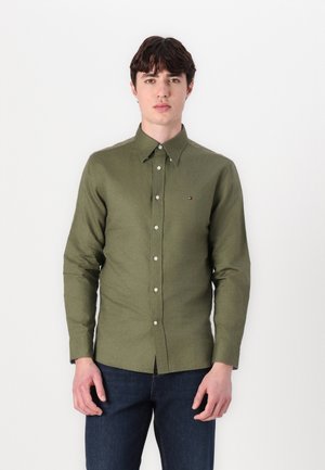 Cămașă butonată de culoare verde măslin, cu mâneci lungi, ajustată, confecționată dintr-un material moale. Prezintă un logo mic pe piept și un design clasic al gulerului.