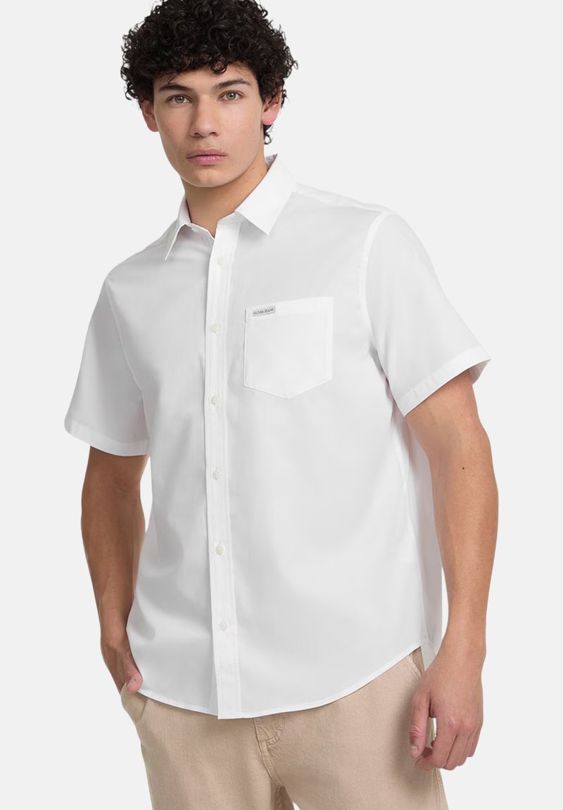 Korte mouwen witte blouse gemaakt van soepel stof, met een borstzak en een label boven de zak, en een afgeronde zoom.