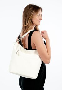 Borsa tote bianca in pelle con texture liscia, dotata di un accento in metallo argentato e una tracolla regolabile, mostrata sulla spalla di una persona.