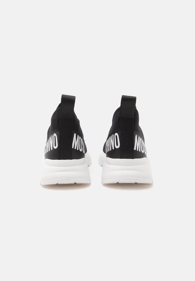 Ζευγάρι μαύρα και λευκά slip-on αθλητικά παπούτσια με χοντρές λευκές σόλες, μαύρες θηλιές και λευκή γραμματοσειρά στο πίσω μέρος.