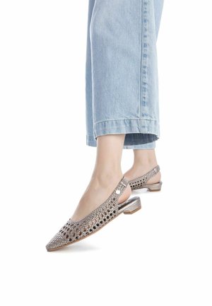 Bailarinas plateadas con diseño abierto, que cuentan con una parte superior de malla, tacón bajo y recortes decorativos, combinadas con jeans de color azul claro.
