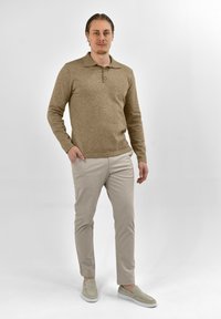 Tan gebreide polo met lange mouwen, een kraag en drie knopen, gecombineerd met lichtbeige slim-fit broeken en grijze instappers.