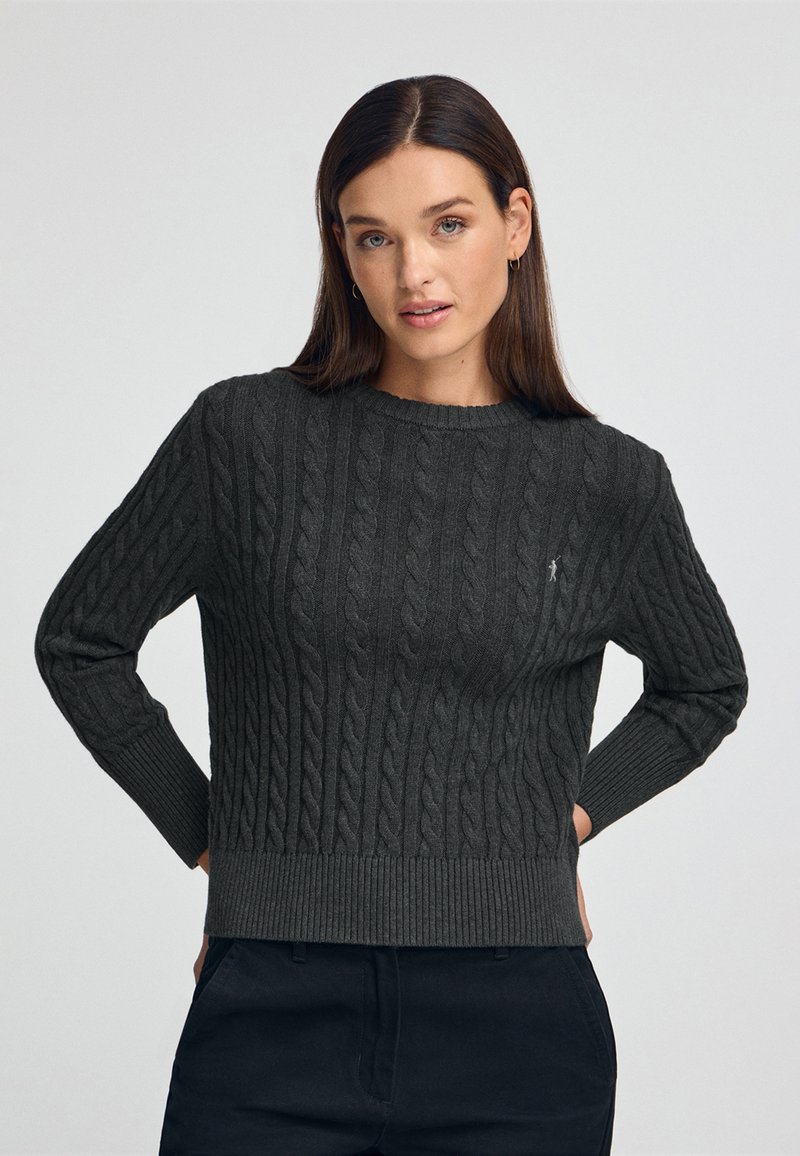 Pull en maille torsadée gris sombre avec des poignets et un ourlet côtelés. Dispose d'un col rond et d'un petit logo en accent sur le devant.