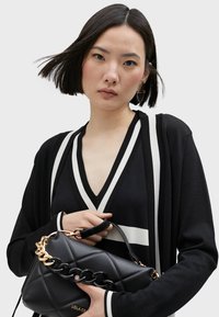 Black and white striped deep V-neck top paired with a black quilted handbag featuring a gold chain strap. Smooth texture, modern design.