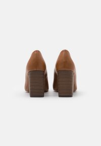 Chaussures à talons hauts en cuir marron avec un bout pointu et un talon bloc texturé. Elles présentent une surface lisse et des détails de couture sur les côtés.