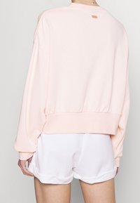 Person wearing pale pink oversized sweatshirt with small orange Nike logo on back and white rolled-hem shorts, facing away from camera.