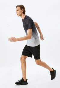 Ropa de running que incluye una camiseta de manga corta en gris degradado y pantalones cortos negros, hechos de un tejido ligero con una textura suave y un pequeño detalle de logo.